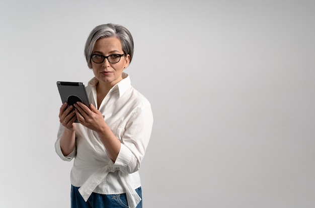 De mooie grijzende onderneemster houdt digitale tablet terwijl het stellen