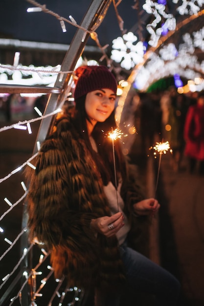 De mooie jonge dame die zich dichtbij Kerstmarkt bevindt met fonkelingen in haar handen