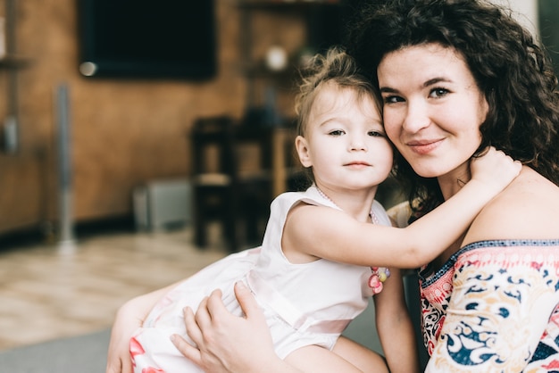 De mooie jonge moeder en haar dochter koesteren thuis en glimlachen