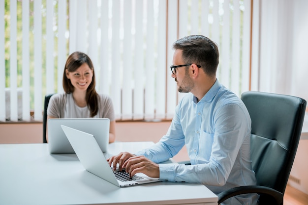 De mooie jonge partners gebruiken laptop, bespreken project en glimlachen terwijl het werken in bureau.