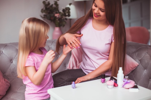 De mooie jonge vrouw en het kleine meisje kijken naar hun manicure moeder en dochter in roze t-shirts zitten in de kamer en zijn bezig met hun schoonheid