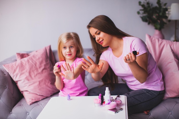 De mooie jonge vrouw en het kleine meisje kijken naar hun manicure Moeder en dochter in roze T-shirts zitten in de kamer en zijn bezig met hun schoonheid