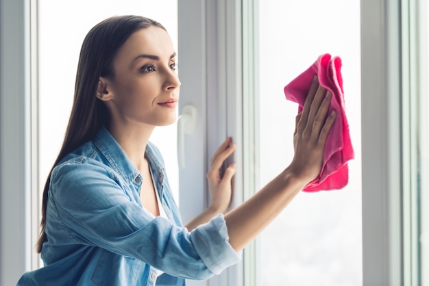 De mooie jonge vrouw gebruikt een vod terwijl het schoonmaken van vensters