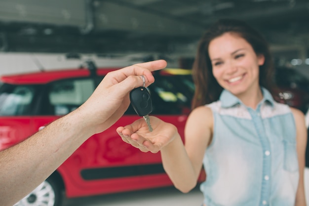 De mooie jonge vrouw houdt een sleutel in autodealer