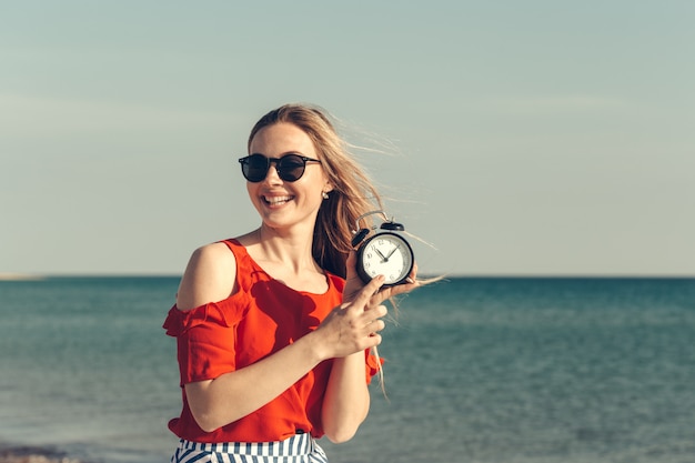 De mooie jonge vrouw houdt wekker op de zomervakantie.