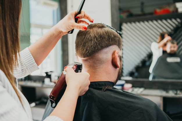 De mooie meisjeskapper snijdt een gebaarde man in de salon