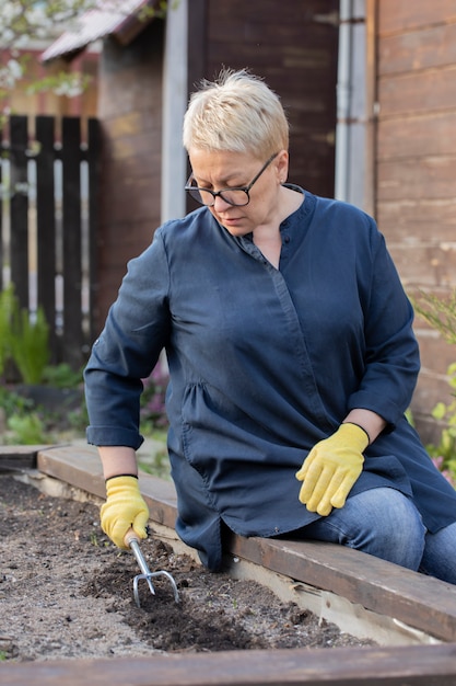 De mooie rijpe vrouw maakt vruchtbare grond los met culti-schoffel alvorens zaden te planten