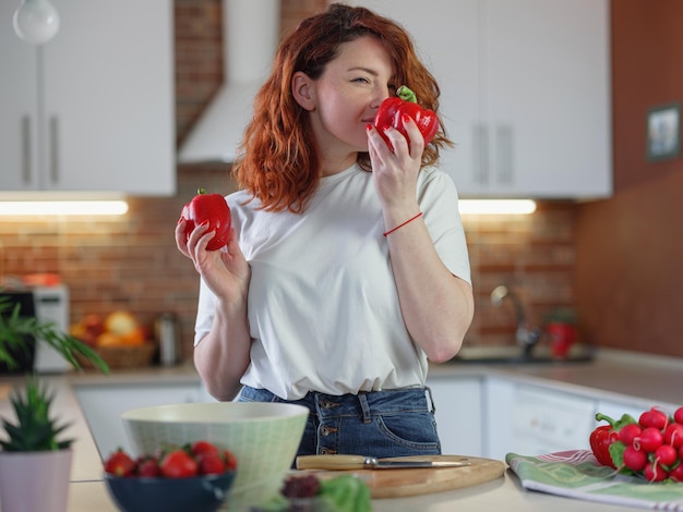 De mooie roodharige jonge vrouw bereidt groentesalade in de keuken voor
