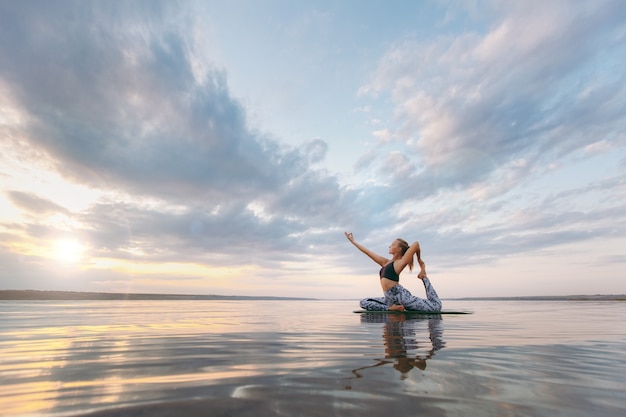 De mooie vrouw die yoga doet bij zonsondergang buitenshuis