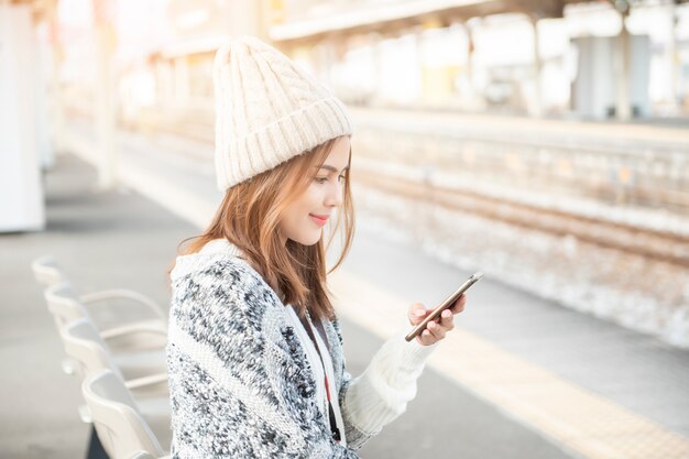 De mooie vrouw gebruikt slimme telefoon op spoorwegplatform