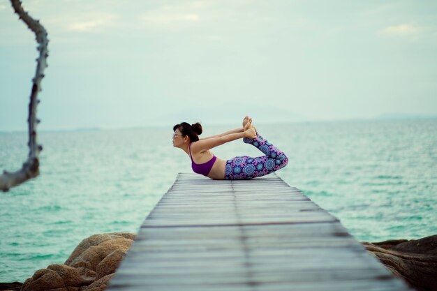De mooie vrouw het spelen yoga in schildpad stelt op overzeese houten pijler