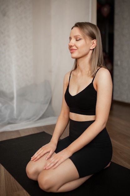 De mooie vrouw houdt zich thuis bezig met meditatie zittend op een zwart tapijt in zwarte kleren