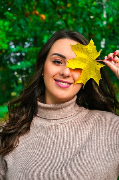 De mooie vrouw in de herfstpark met esdoornblad. Herfst concept. Natuurlijke vrouw met kleurrijk herfstblad in fel zonlicht