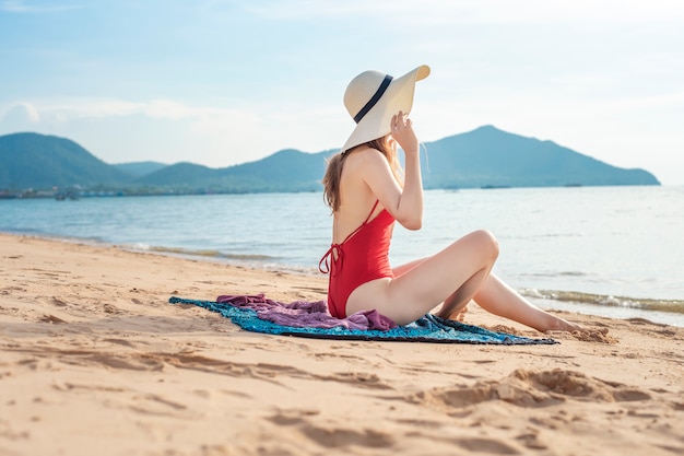 De mooie vrouw in rood zwempak zit op het strand