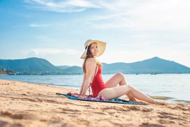 De mooie vrouw in rood zwempak zit op het strand