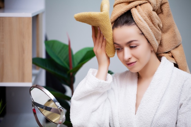 De mooie vrouw in witte laag veegt gezicht met handdoek na douche af