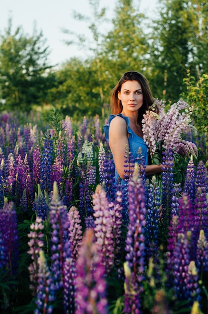 De mooie vrouw kleedde zich in een kleding in bloemenlupines bij zonsondergang