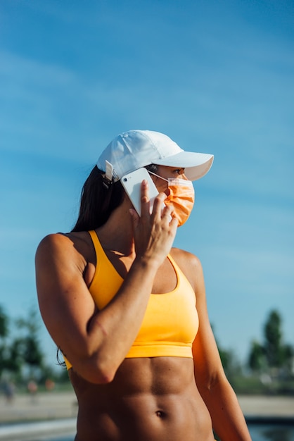 De mooie vrouw kleedde zich in sporten met masker gebruikend mobiele celtelefoon.