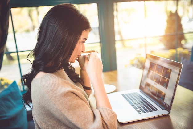 De mooie vrouw met een laptop drinkt een kopje koffie in een café