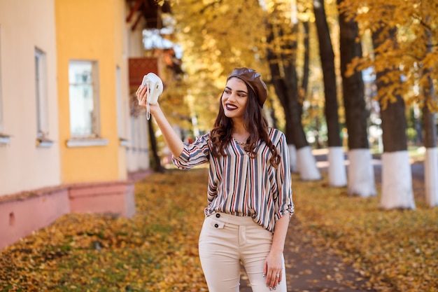 De mooie vrouw neemt foto's gebruikend instaxcamera. Herfst tijd