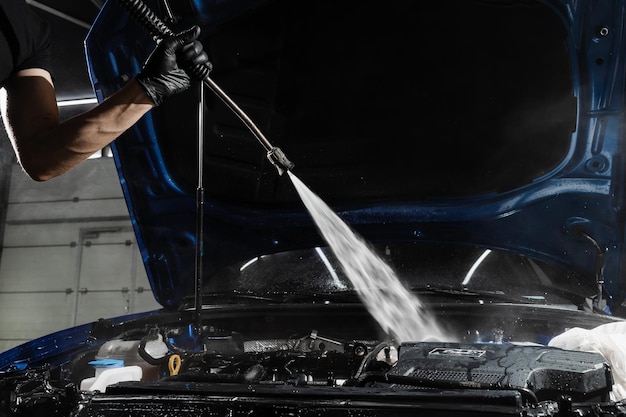 De motor van een auto wassen met met water in detaillering van autoservice Detaillering van de motor van stof en vuil Gieten van water op de motor van een auto