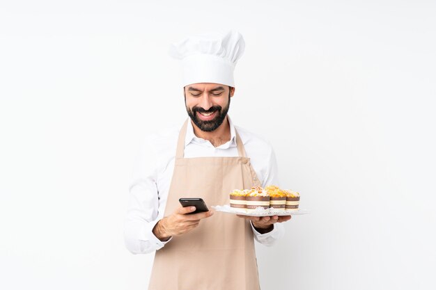 De muffincake van de jonge mensenholding over geïsoleerd wit die een bericht met mobiel verzenden