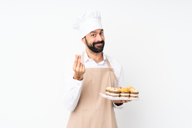 De muffincake van de jonge mensenholding over geïsoleerde witte muur die geldgebaar maken