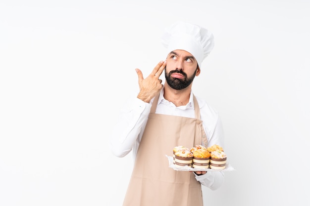 De muffincake van de jonge mensenholding over geïsoleerde witte muur met problemen die zelfmoordgebaar maken