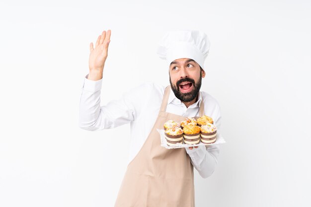 De muffincake van de jonge mensenholding over geïsoleerde witte zenuwachtig en doen schrikken muur