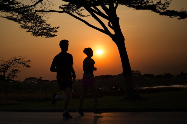 De oefeningsjogging van het silhouetpaar in park bij avondzonsondergang