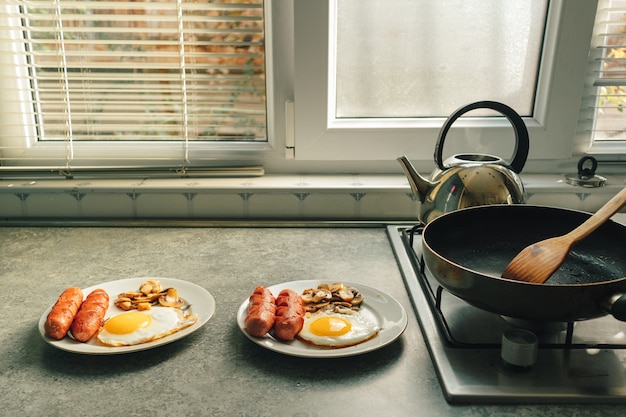 De ontbijtreeks worsten braadde eieren en paddestoel op het aanrecht in warm ochtendlicht.