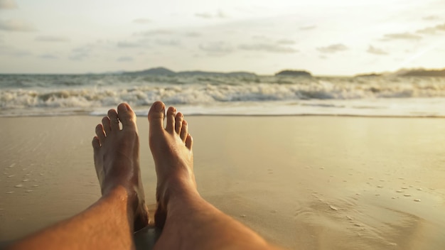 De ontspannen voeten van de man liggen op het zandstrand en worden gewassen door het water en het schuim van de oceaan