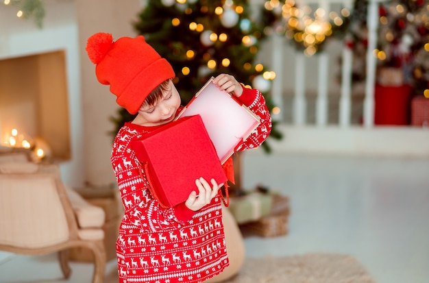 De opening van het kind is aanwezig bij de kerstboom thuis Jongen in rode pyjama met cadeautjes
