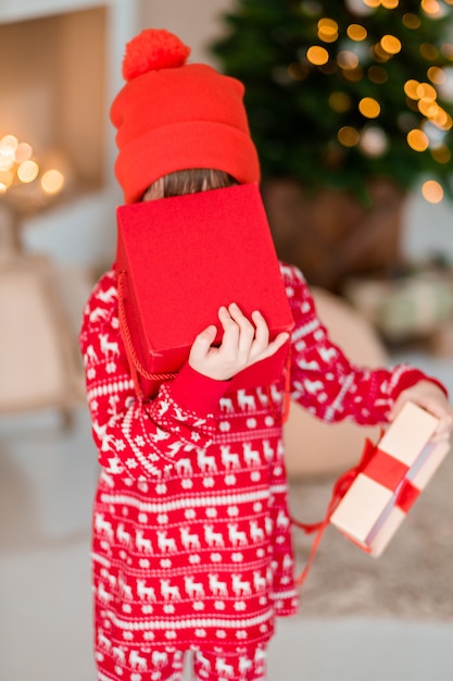 De opening van het kind is aanwezig bij de kerstboom thuis jongen in rode pyjama