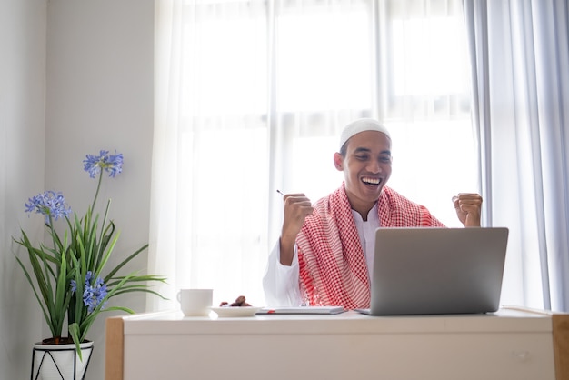 De opgewekte succeszakenman heft zijn wapen op tijdens het gebruik van laptop