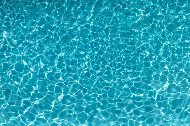 De opwinding van het water in het zwembad De textuur van het oppervlak van het blauwe zwembad de achtergrond van het water in het zwembad met kopieerruimte van de schittering van de zon