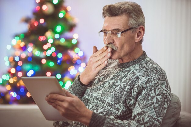 De oude man met een tablet voert een videogesprek bij de kerstboom