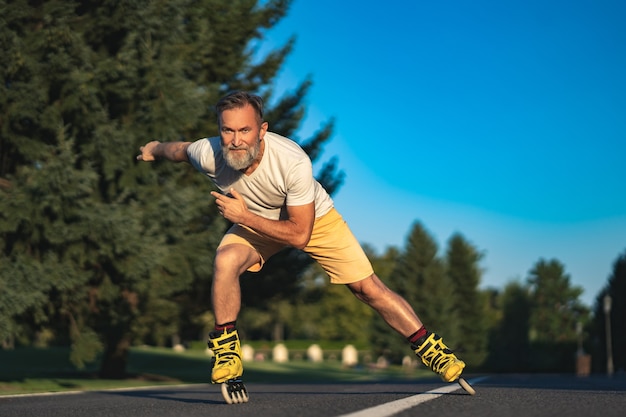 De oude man rolschaatsend op de weg