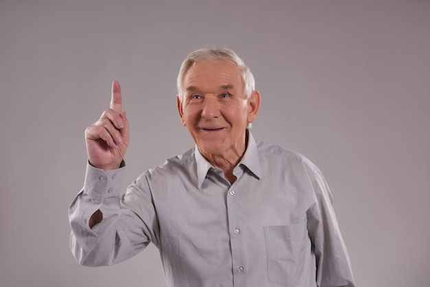 De oude mens staat met geïndexeerde vinger op grijs op.