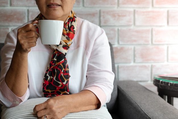 De oude vrouw houdt thuis een kop van hete koffiedrank