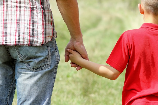 De ouder houdt de hand van een klein kind vast op de natuur