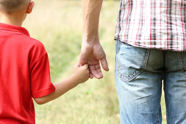 De ouder houdt de hand van een klein kind vast op de natuur