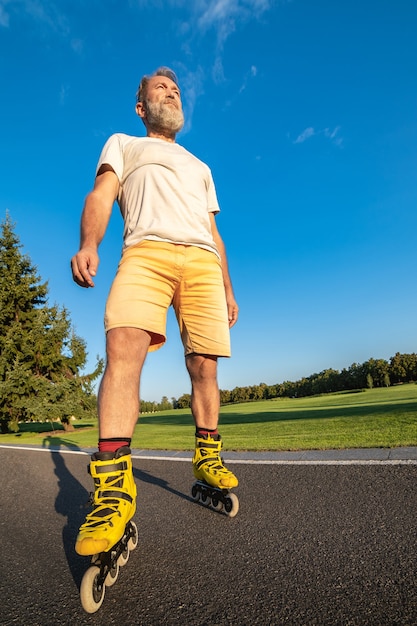 De oudere man in rollen die op de weg staat