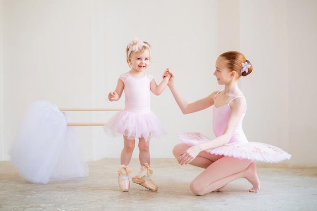 De oudere zus, een ballerina in een roze tutu en spitzen, laat de baby zien hoe ze aan de barre moet oefenen