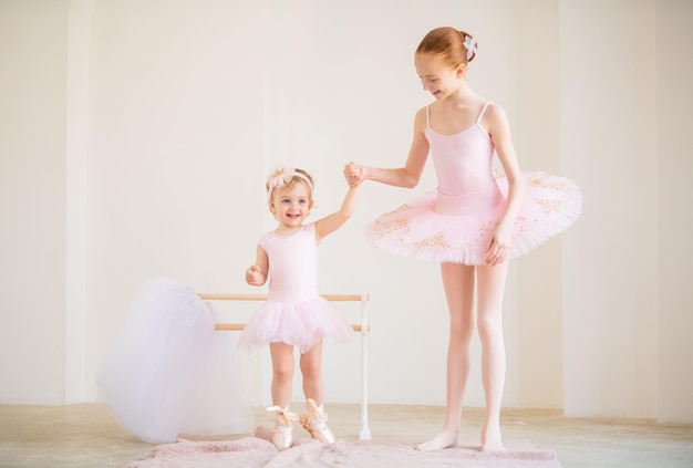 Foto de oudere zus, een ballerina in een roze tutu en spitzen, laat de baby zien hoe ze aan de barre moet oefenen