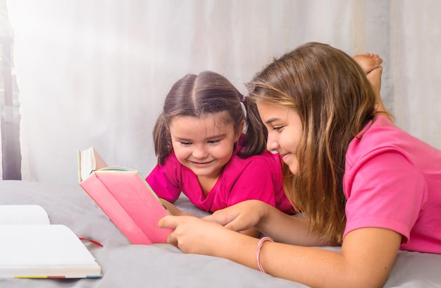 De oudere zus helpt de jongere een boek te lezen terwijl ze op bed ligt