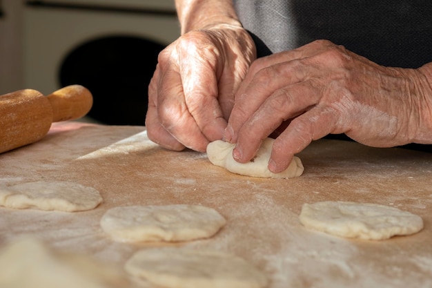 De overwerkte handen van de oude vrouw maken taarten van deeg. Handgemaakt huiswerk met gebakken goederen.
