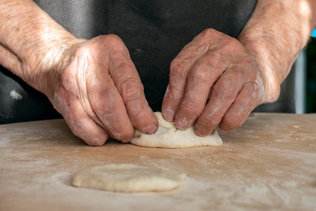 Foto de overwerkte handen van de oude vrouw maken taarten van deeg.