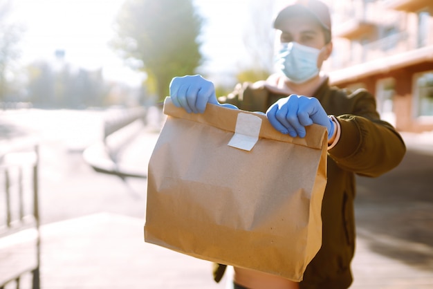 De papieren zak met eten en koffie in de handen van de koerier in quarantaine stad. Bezorgservice onder quarantaine, ziekte-uitbraak, coronavirus covid-19 pandemische aandoeningen.