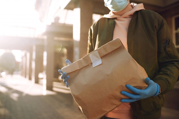 De papieren zak met eten en koffie in de handen van de koerier in quarantaine stad. Bezorgservice onder quarantaine, ziekte-uitbraak, coronavirus covid-19 pandemische aandoeningen.